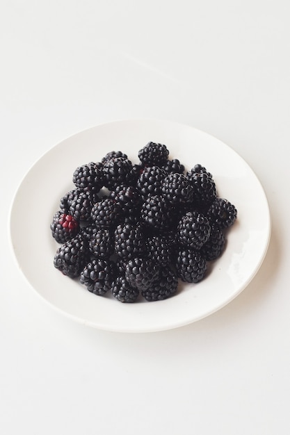 Photo fresh blackberries in two white cups on white background