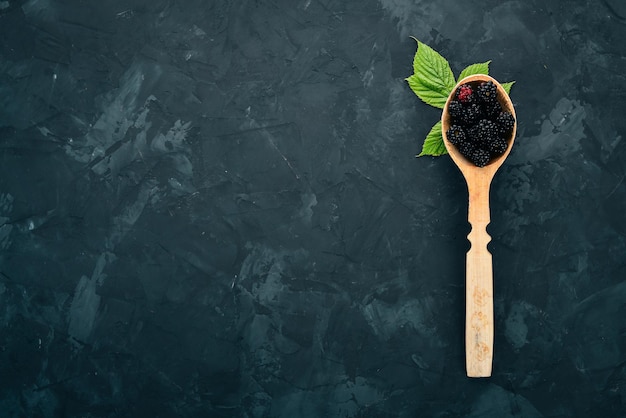 Fresh blackberry in a spoon on a black stone background top view free space for text