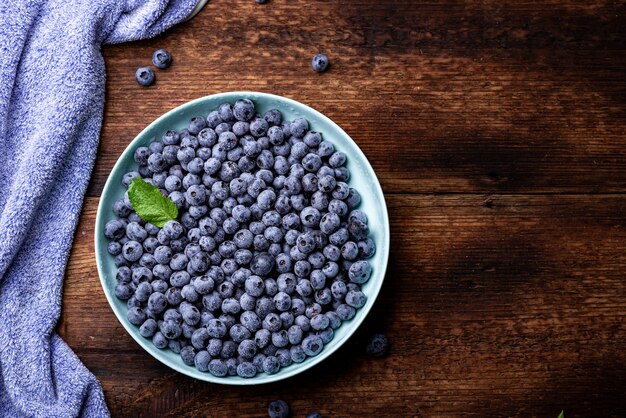 Fresh blueberries berries in a plate on a dark wooden background.