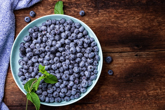 Fresh blueberries berries in a plate on a dark wooden background