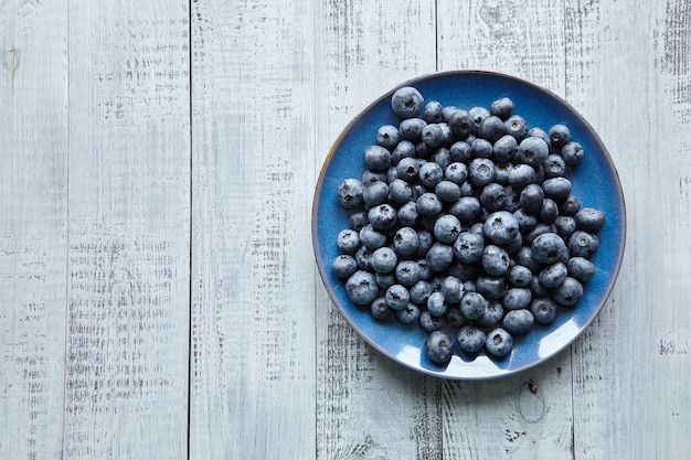 Fresh blueberries on blue plate on wooden table top view