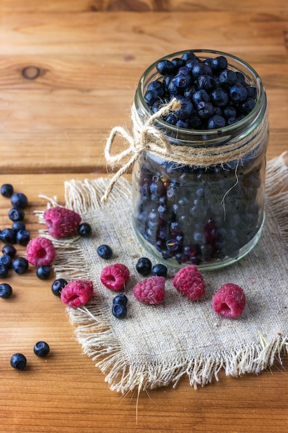 Fresh blueberries in a jar and raspberries on the table.