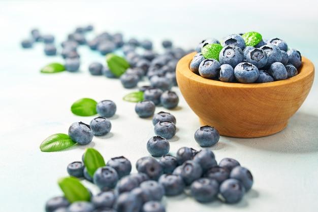 Fresh blueberries  with green leaves in a wooden bowl on a light background, with copy space.