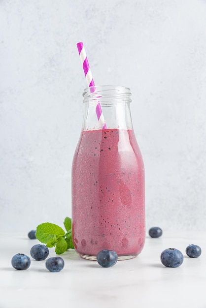 Fresh blueberry smoothie in a glass bottle with straw and mint on white background Summer refreshing drink