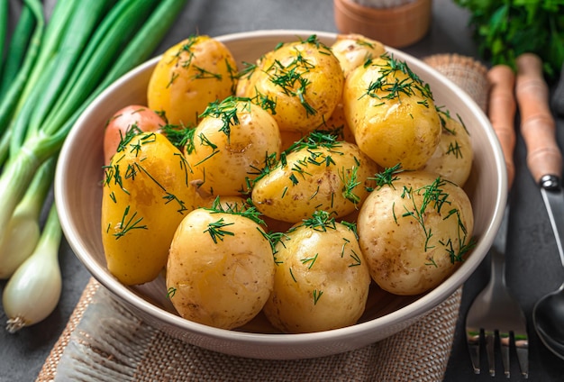 Fresh boiled young unpeeled potatoes with dill and butter on a dark background with dill and spices
