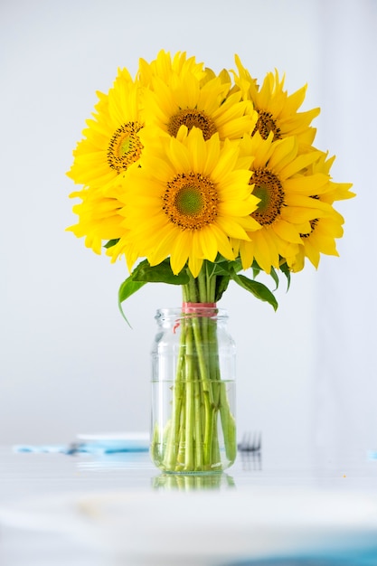 Fresh bouquet of daisy sunflowers in glass vase on white table Summer flowers at home interior