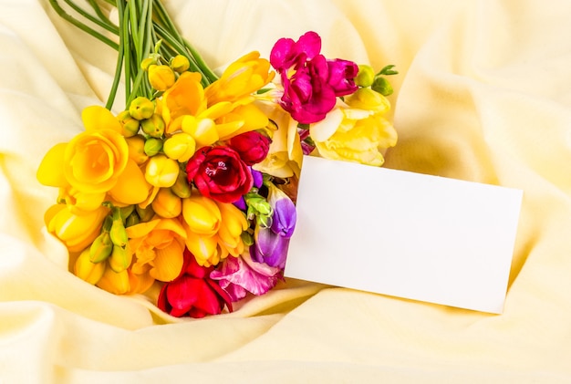 노란색 실크 배경에 신선한 프리지아 꽃다발과 빈 카드