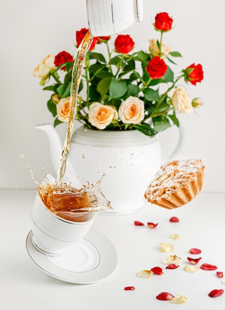 Fresh bouquet of roses, flying cupcake and splashing tea