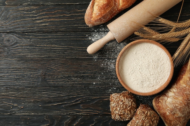 Fresh bread, flour, spikelets and rolling pin on wooden background