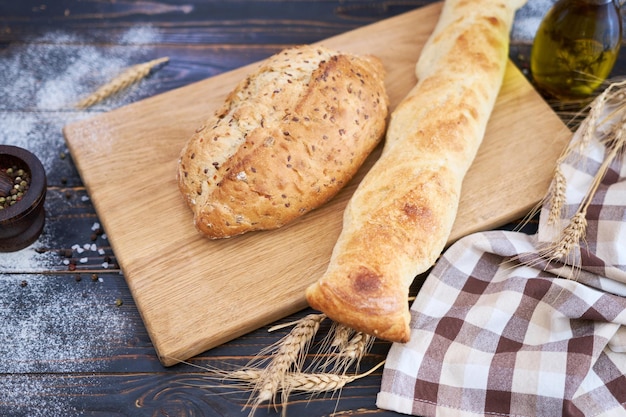 Fresh bread loaf and baguette on wooden cutting board at kitchen table