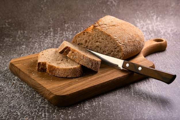 Fresh bread slice and cutting knife on wooden cutting board