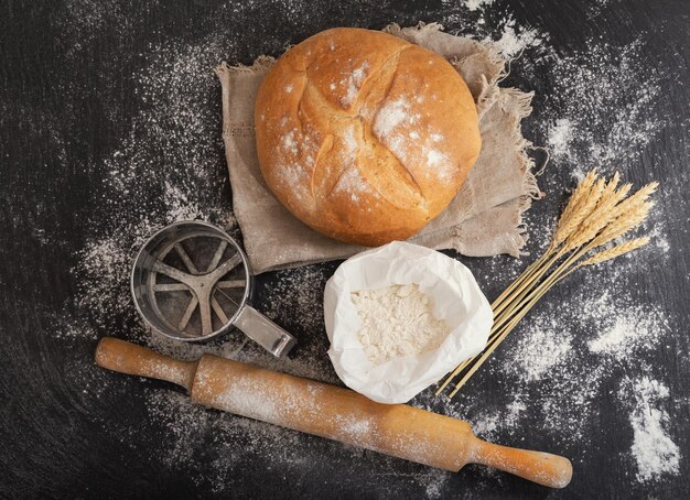 Fresh bread with wheat ears flour and kitchen utensils on dark board