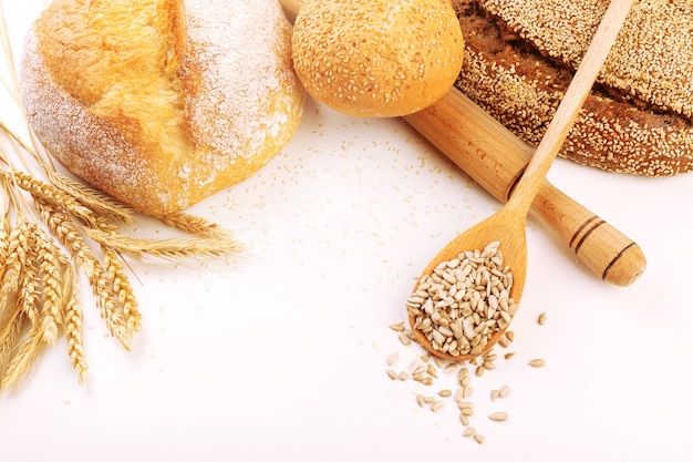 Fresh bread with wheat and wooden spoon of sunflower seeds on white