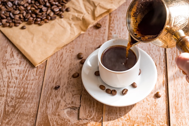 Fresh breved coffee in cezve Woman's hand pours coffee into white cup