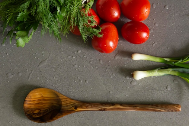 Fresh bright fragrant vegetables and a bamboo spoon lie on the gray kitchen