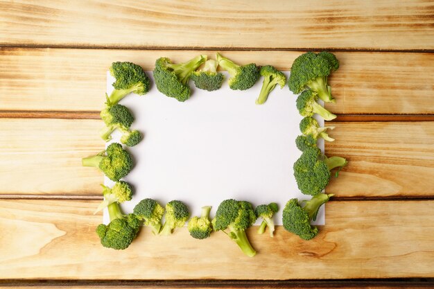 Foto broccoli freschi e foglio bianco in bianco su fondo di legno.