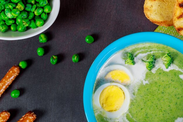 Fresh broccoli cream soup and cooked chicken eggs with bread in bowl.