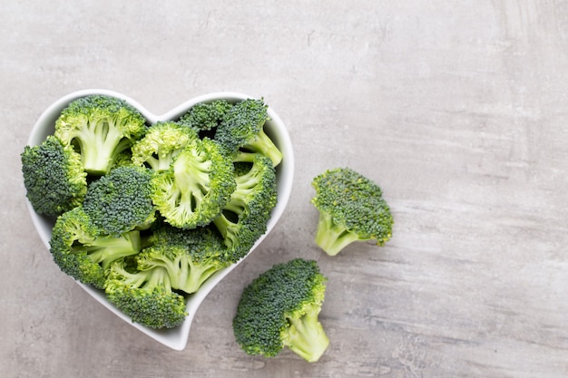 Fresh broccoli in a heart shaped bowl on a wooden background.