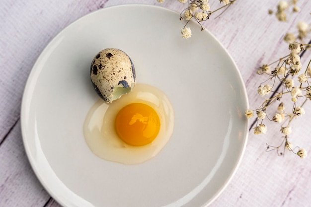 Fresh broken quail egg yolk and white on a white plate