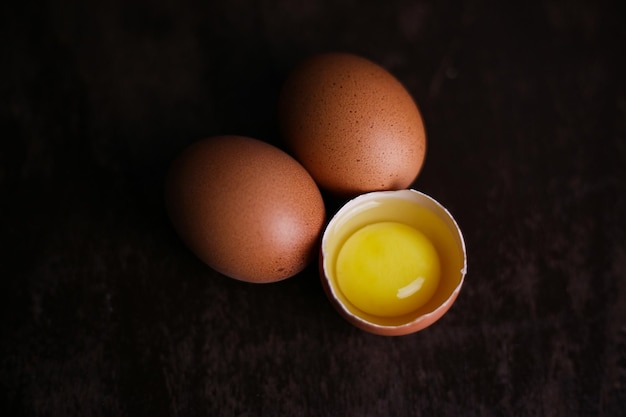 Fresh brown eggs and a broken egg with yolk on a dark wooden background