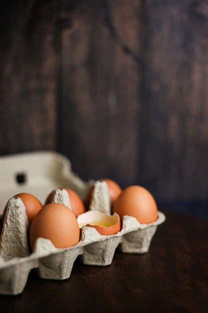 Fresh brown eggs and a broken egg with yolk in an eco tray made from recycled paper on a dark wooden