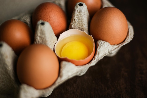 Fresh brown eggs and a broken egg with yolk in an eco tray made from recycled paper on a dark wooden