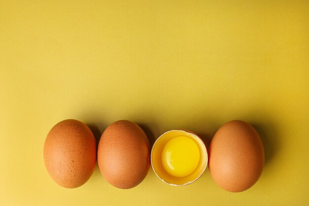 Fresh brown eggs and a broken egg with yolk on a light yellow background with space for text