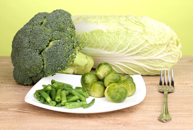 Fresh brussels sprouts and french bean on plate on wooden table on green background