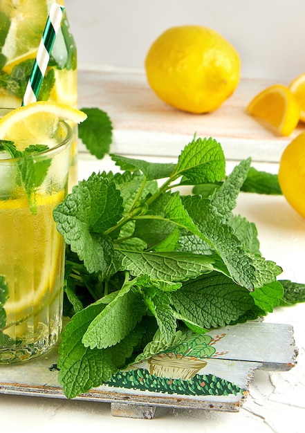 Fresh bunch of mint and a glass with lemonade on a wooden board