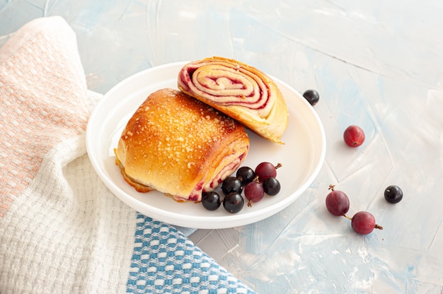 Fresh buns with berry filling decorated with black currants and\
gooseberry on a light blue concrete background.