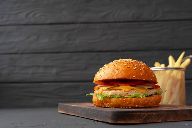 Fresh burger and fries on black wooden background, front view