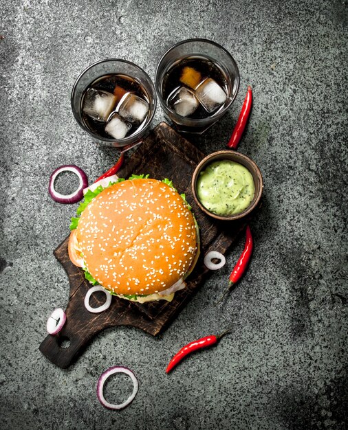 Fresh burger with cola and hot sauce. On a rustic table.