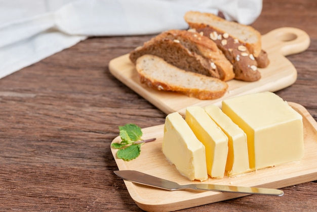 Fresh butter cut with knife on wooden plate and bread.