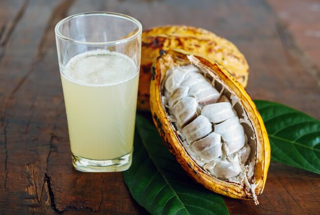 Photo fresh cacao water in glass and half sliced ripe yellow cacao pod with white cocoa seed cacao juice