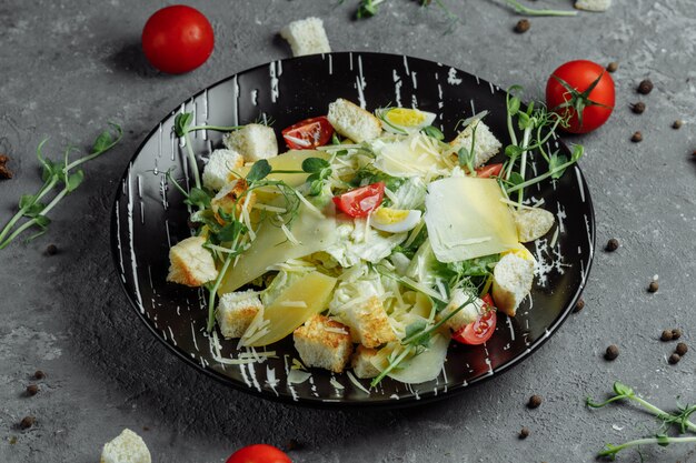 Fresh Caesar salad on a black plate on a gray background