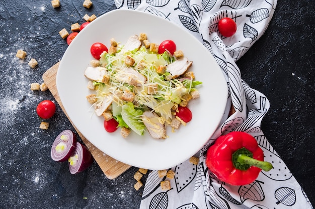 Fresh caesar salad with chicken on a white plate on dark stone. 