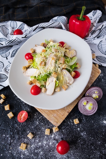 Fresh caesar salad with chicken on a white plate on dark stone. 