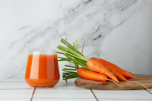 Fresh carrot juice in glass on table and light background with fresh carrot on wooden deck.