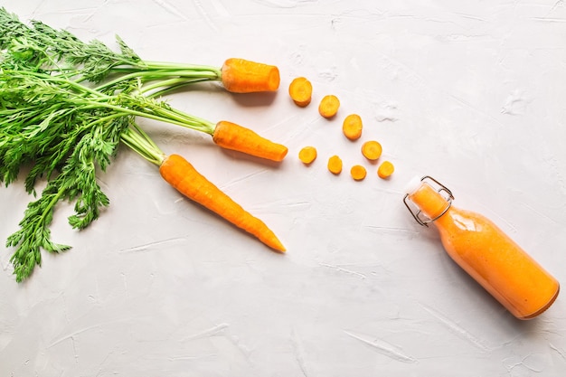 Fresh carrot smoothie in bottle on light concrete.