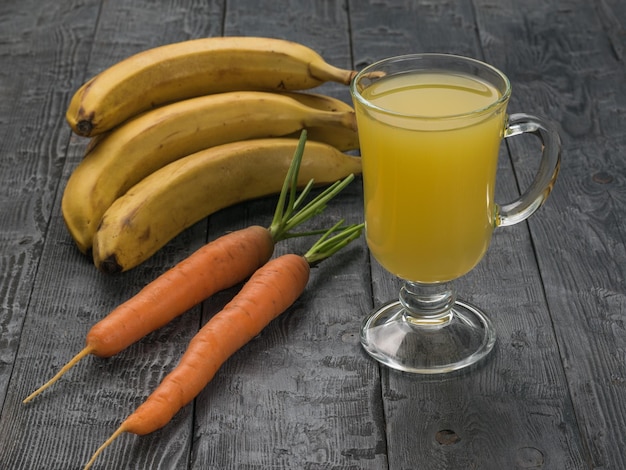 Fresh carrots and bananas and a glass of juice on a wooden table