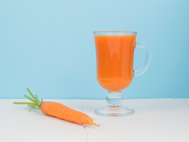 Fresh carrots and orange carrot smoothie on a white wooden table.