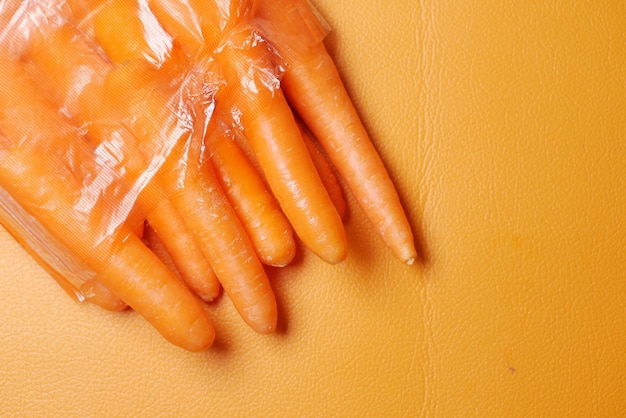 Свежая морковь в полиэтиленовом пакете на оранжевом фоне