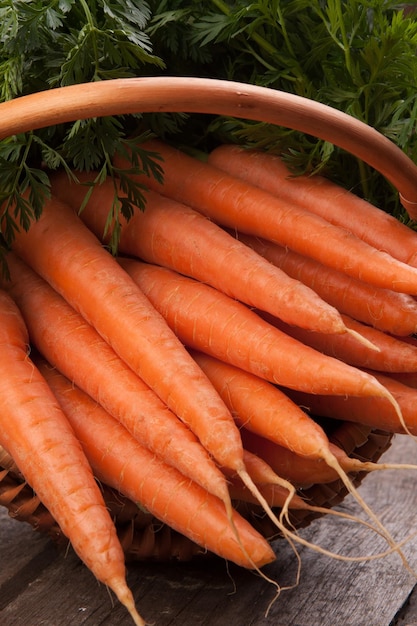 Fresh carrots in wicker basket bunch on grungy wooden background