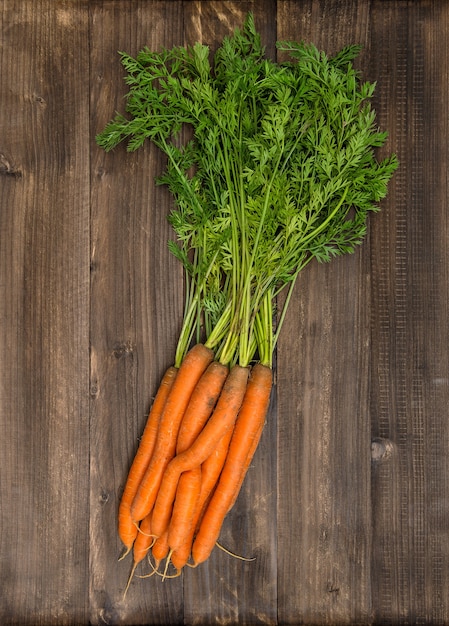 Fresh carrots with green leaves over wooden background. organic food concept