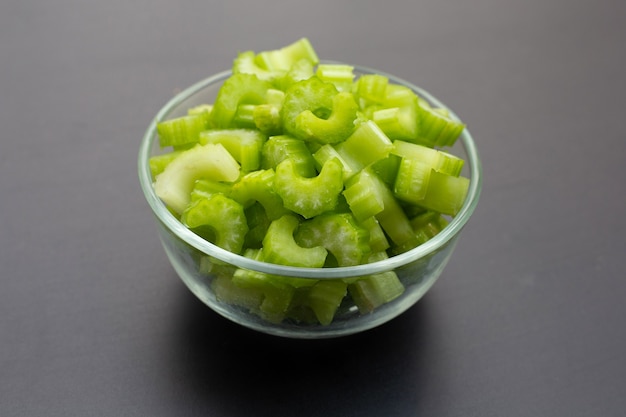 Fresh celery slices in glass bowl on dark wall.