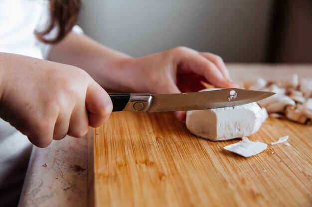 Fresh champignon mushrooms on a wooden board, girl cuts mushrooms with a knife.