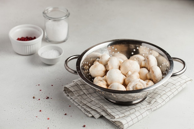 Photo fresh champignon porcini mushrooms in a metal colander, spices in bowls