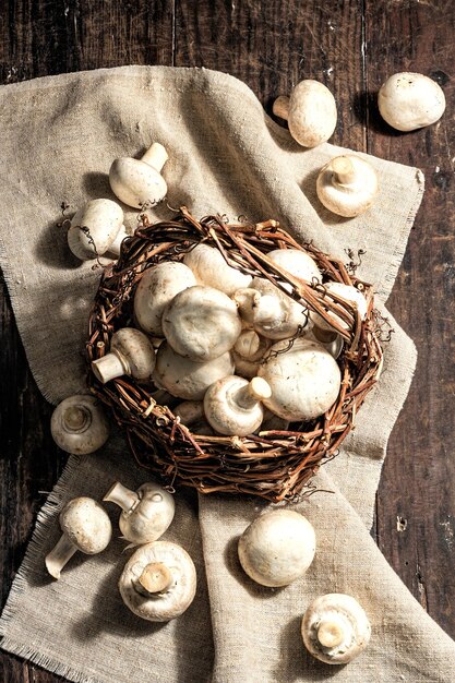 Fresh champignons in a basket. Raw ingredient for cooking vegan food. Old wooden background, fashion hard light, dark shadow, rustic style, top view