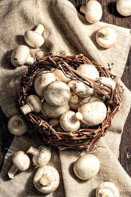 Fresh champignons in a basket. Raw ingredient for cooking vegan food. Old wooden background, fashion hard light, dark shadow, rustic style, top view