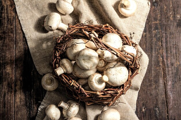 Fresh champignons in a basket. Raw ingredient for cooking vegan food. Old wooden background, fashion hard light, dark shadow, rustic style, top view